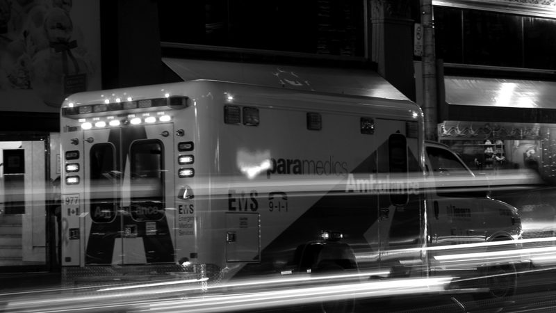 An ambulance at night with light trails, in black and white