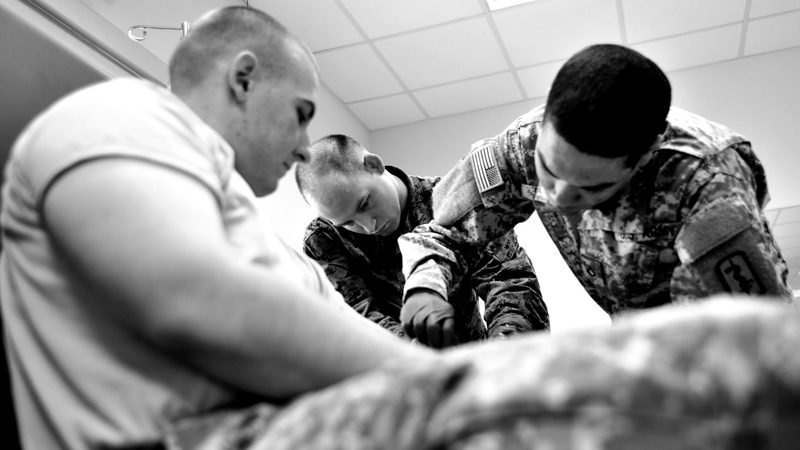 Army medics practising intravenous line placement, in black and white